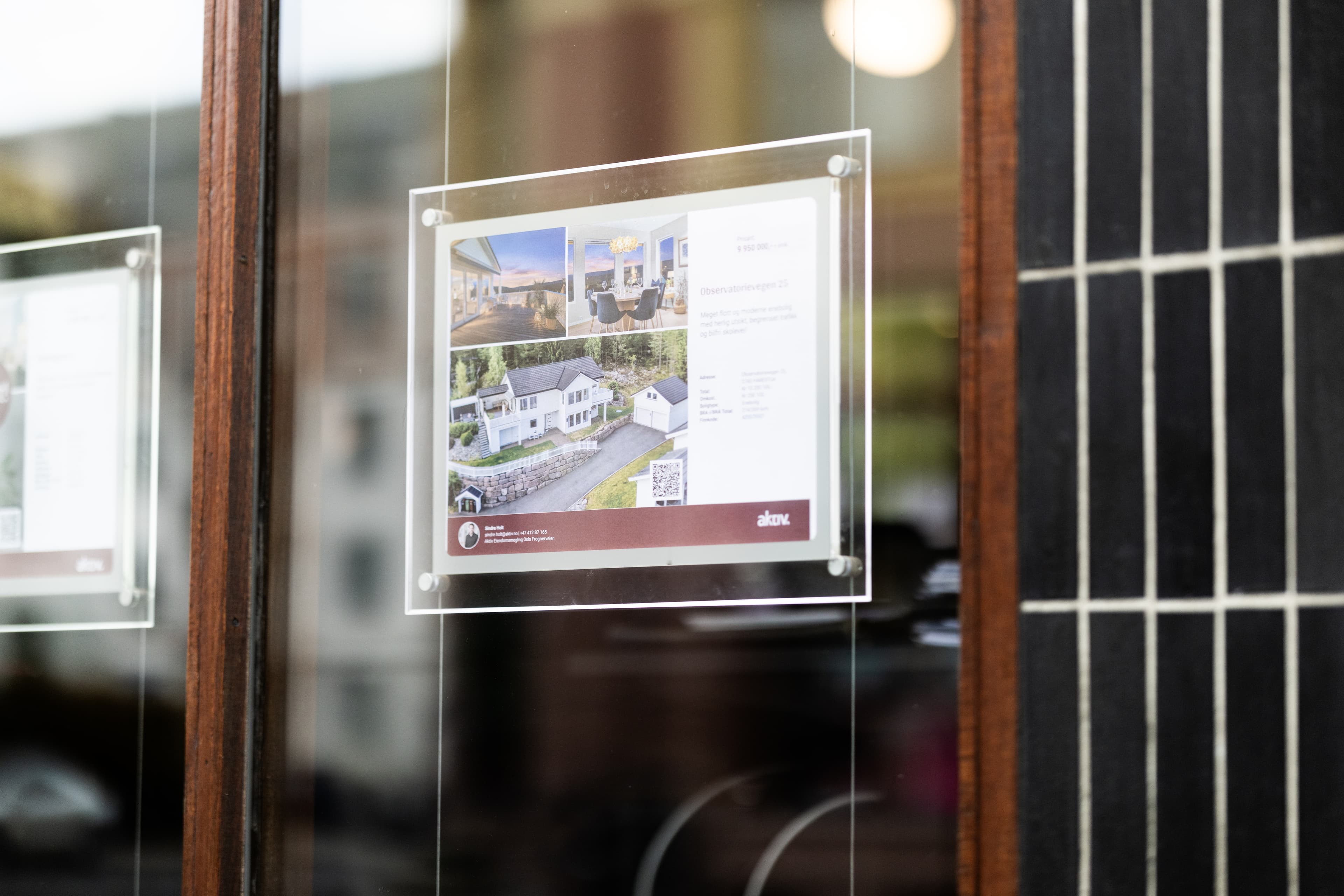 Boligplakat med bilder av hvit enebolig, terrasse og spisestue i vinduet til et meglerkontor, brukt som illustrasjon i artikkel om beste eiendomsmegler på Fosen.